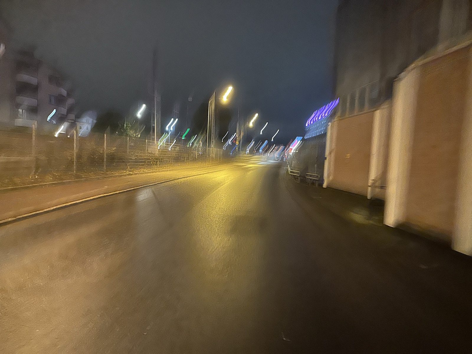 A wet street at night seen on the move, the streetlights pulled into streaks of light ahead